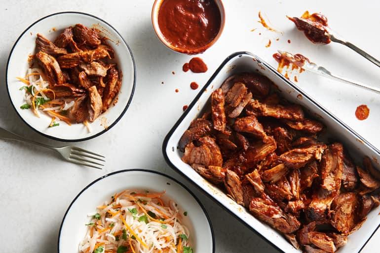 Overhead view of a pan of chipotle pulled pork made with Muir Glen Organic Tomato Sauce next to a bowl of jicama slaw and barbeque sauce.