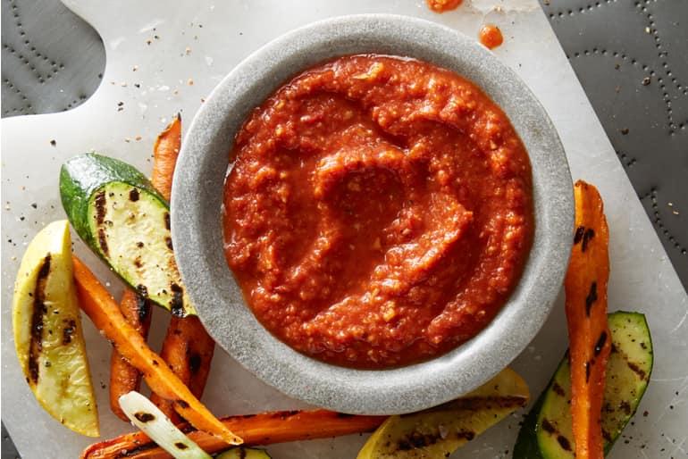 Overhead view of a bowl of smoky romesco sauce made with Muir Glen Organic Fire Roasted Diced Tomatoes, next to grilled mixed vegetables.