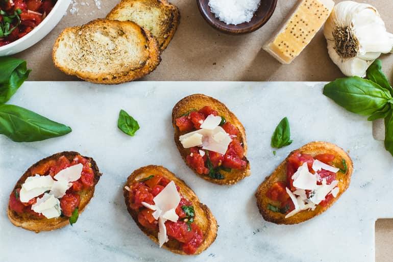 Bruschetta topped with Muir Glen Fire Organic Roasted Diced Tomatoes, parmesan and basil on a marble surface.