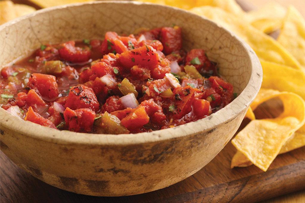 A rustic wooden bowl filled with chunky salsa. Tortilla chips are visible in the background.